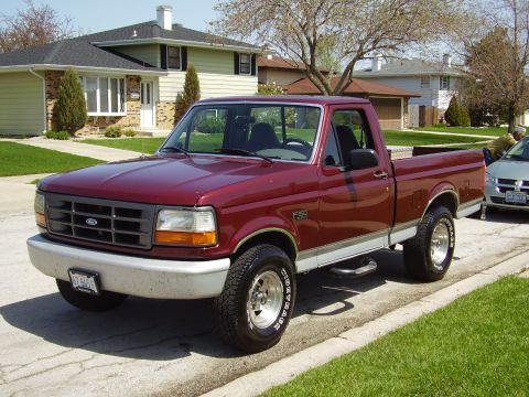 1996 Ford F-150 - A red 1996 Ford F-150 pickup truck is parked on a suburban street with a house in the background.