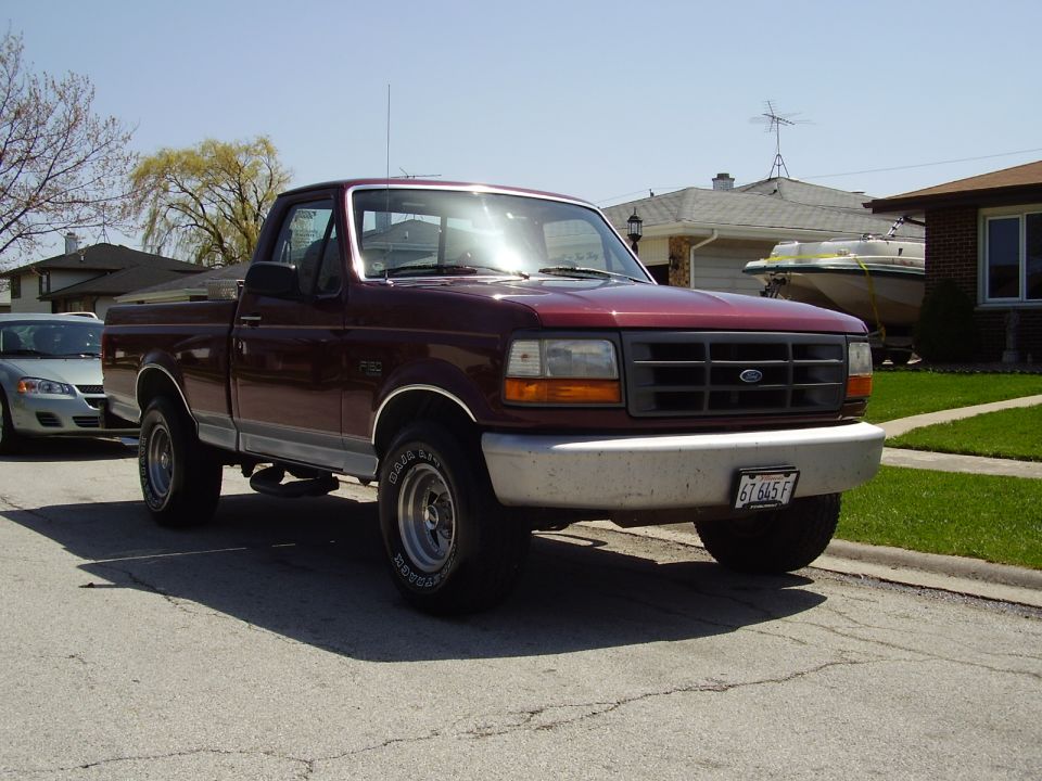 Maroon Ford F-150 pickup truck, front 3/4 view, parked on street, silver car to the left