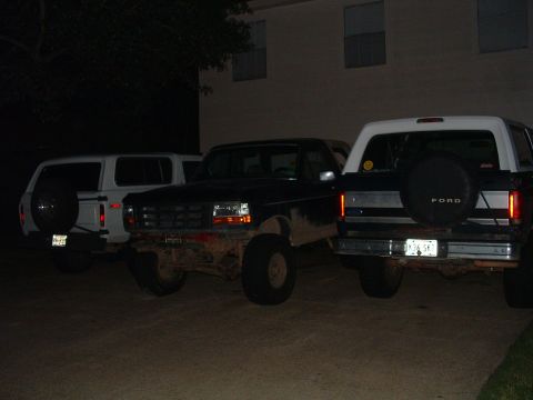 1993 Ford Bronco - Three SUVs are parked in a lot at night, with the rear of a 1993 Ford Bronco prominently featured.