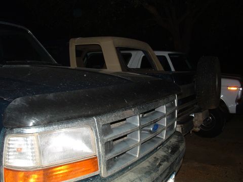 1993 Ford Bronco - Two trucks are parked outside at night, one with a dark blue exterior and the other with a tan top.