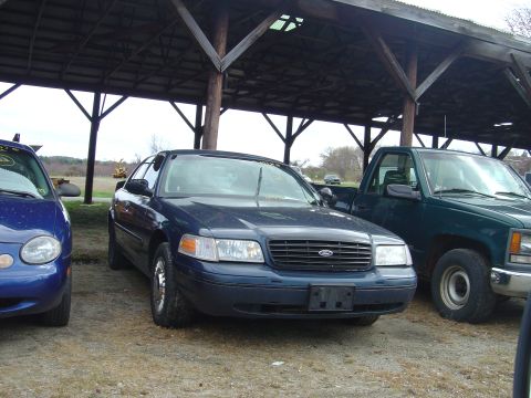 2001 Ford Crown Victoria - A dark blue 2001 Ford Crown Victoria is parked under a covered structure, alongside other vehicles.