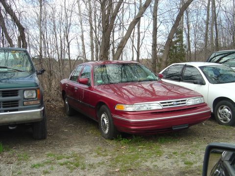 2001 Ford Crown Victoria - A red 2001 Ford Crown Victoria sedan is parked outdoors next to other vehicles.