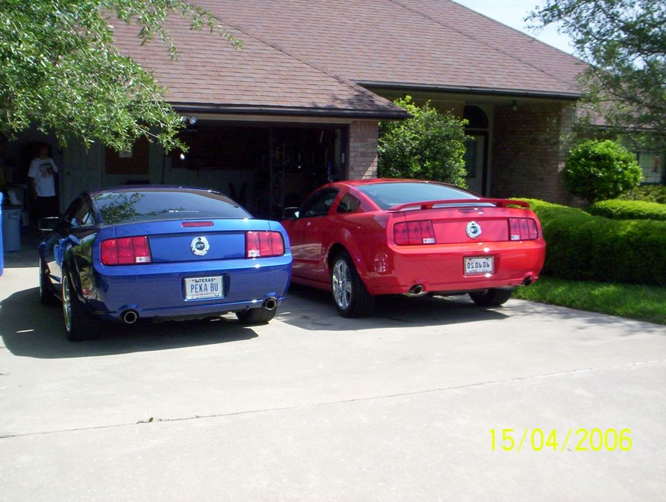 Two Ford Mustangs, one blue and one red, parked in a driveway in front of a house