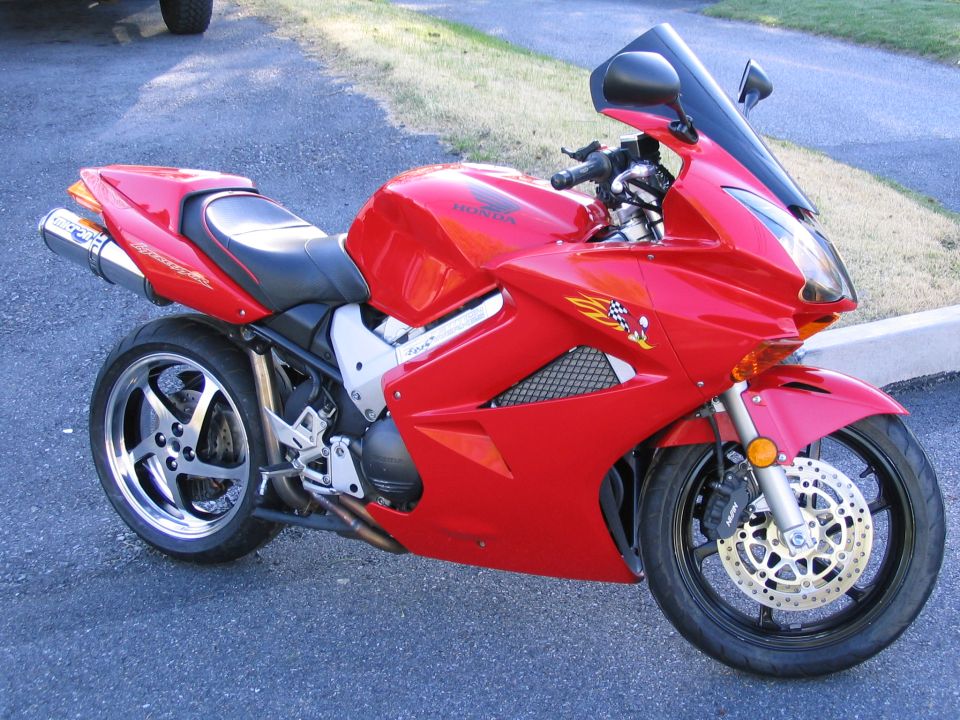 Red Honda VFR sportbike on side stand, right side view with aftermarket slip-on exhaust