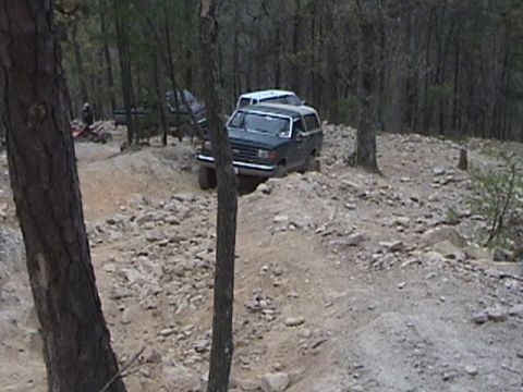 1996 Ford Bronco - Two SUVs navigate a challenging off-road course in a wooded area.