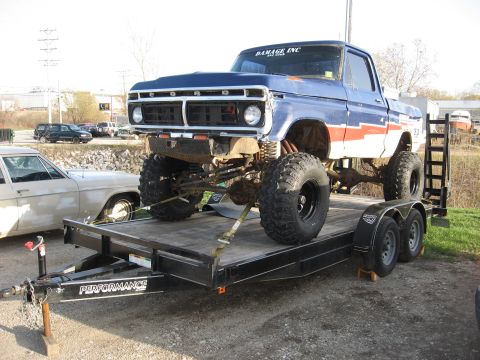 1977 Ford F-150 - This lifted pickup truck is being transported on a trailer, large off-road tires and a custom front bumper.
