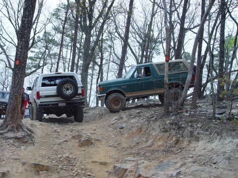 1996 Ford Bronco - Two Ford Broncos navigate a challenging rocky trail in a wooded area.