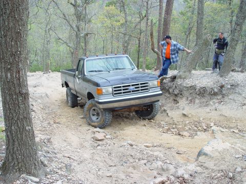 1996 Ford Bronco - A lifted Ford pickup truck navigates a rough, wooded trail with two onlookers.