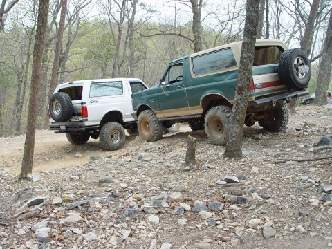 1996 Ford Bronco - Two Ford Broncos navigate a rocky, wooded trail.