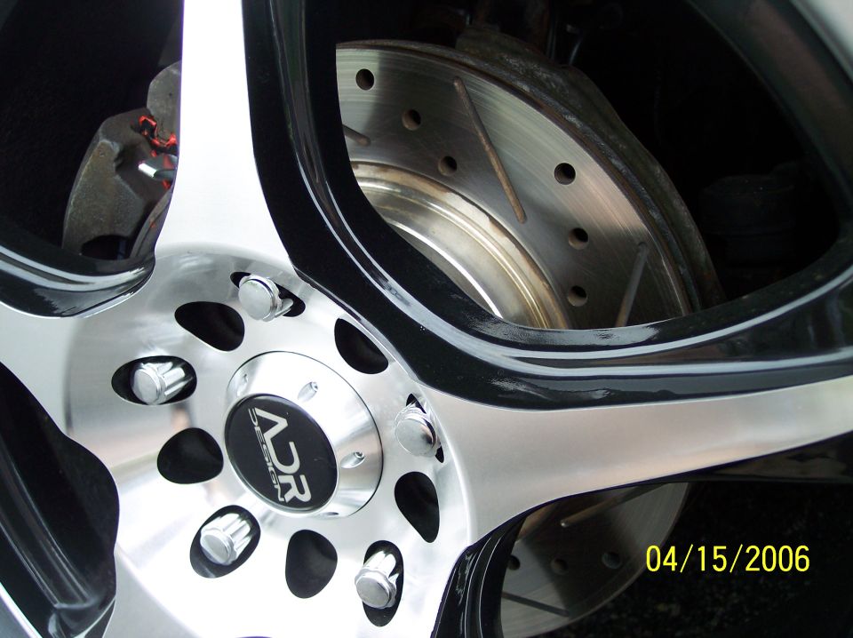 Close-up of a car's front wheel with a drilled brake rotor and 'ADR Designs' center cap. Date stamp reads 04/15/2006
