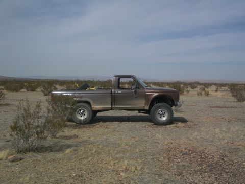 1985 Ford Ranger - Side view of a brown 1985 Ford Ranger pickup truck in a dry, brush-filled landscape under a cloudy sky.