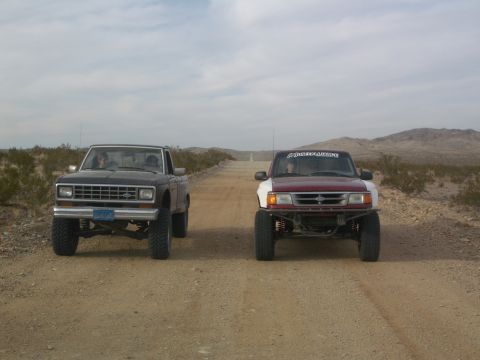 1985 Ford Ranger - Two Ford Rangers drive down a dusty desert road under a cloudy sky.