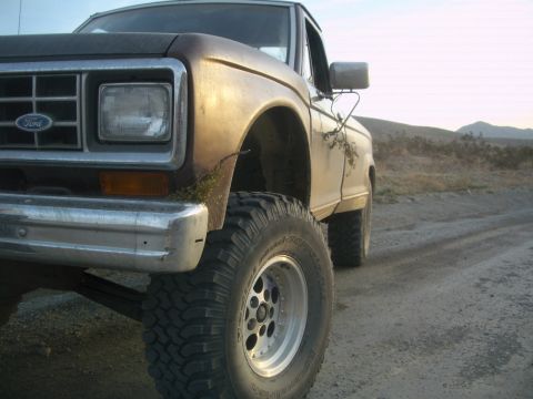 1985 Ford Ranger - This lifted Ford pickup truck is parked on a dirt road with hills in the background.