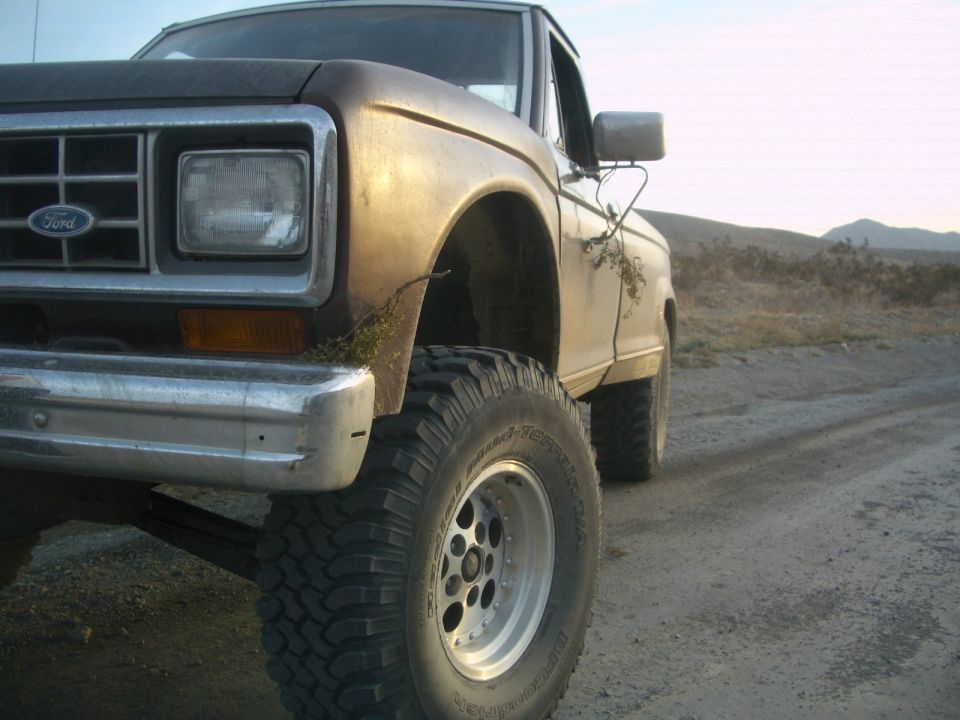 Close-up of a lifted Ford pickup truck with large tires on a dirt road