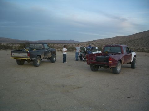 1985 Ford Ranger - Several trucks are parked in a dusty, arid environment with hills in the background.
