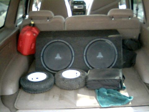 1999 Ford Explorer - The cargo area of a vehicle contains a dual subwoofer box, two spare tires, and a red gas can.