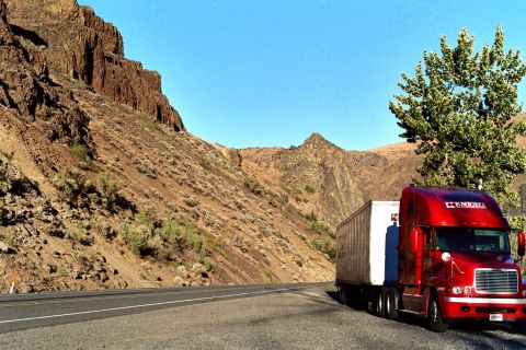 1979 Ford Bronco - A red semi-truck and trailer travels down a highway beside a mountain landscape.