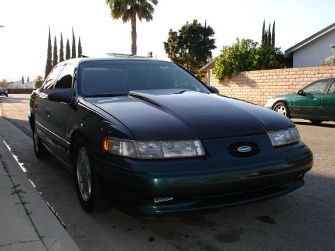 1993 Ford Taurus - 1993 Ford Taurus, a dark green sedan with a custom scooped hood, parked curbside.