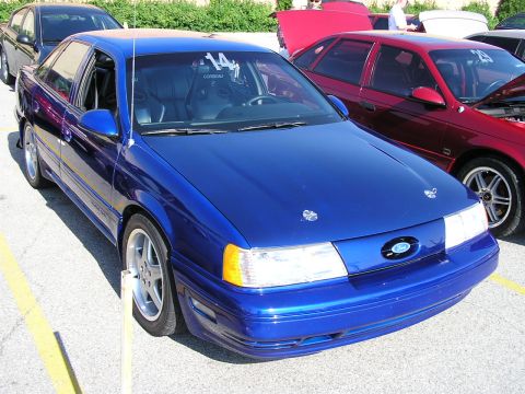 1993 Ford Taurus - A blue 1993 Ford Taurus is parked next to a red car, with racing seats visible inside the blue vehicle.