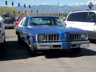 1972 Ford Ranchero - A blue Pontiac sedan with a distinctive grille is parked in a lot, with mountains visible in the distance.