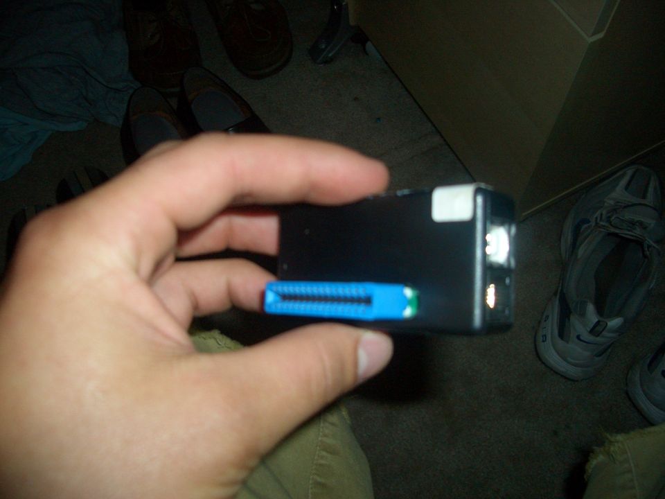 Hand holding black digital camera with blue SD card slot; Supermotors.net logo at bottom right