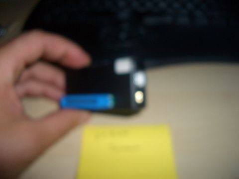 1990 Ford Bronco - A hand holds a small electronic device with a blue battery pack, with a yellow note in the background.