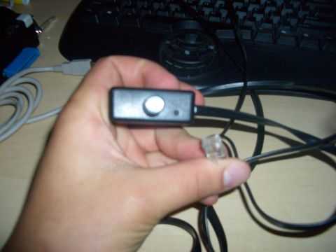 1990 Ford Bronco - A hand holds a small electronic device with a knob and LED, connected to cables, with a keyboard visible.