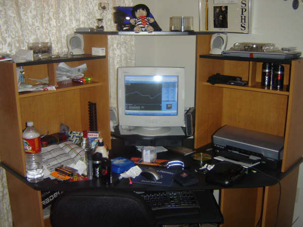 Desk setup with CRT monitor displaying a graph, keyboard, printer, and shelves with bottles and other items