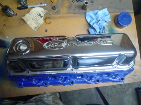 1984 Ford Bronco - Chrome 'Ford Racing' embossed valve cover with oil fill hole sitting on a freshly blue-painted cylinder head on a workbench. Valve springs,…