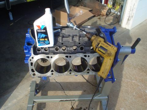 1984 Ford Bronco - A bare V8 engine block painted blue sits on a gray ACDelco engine stand in a garage doorway, with the heads off and four freshly honed cyli…