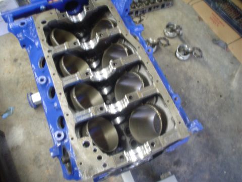 1984 Ford Bronco - Blue-painted Ford V8 engine block with pistons installed and main bearing caps exposed, sitting on a workbench during a rebuild.