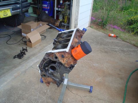 1984 Ford Bronco - Bare V8 short block mounted on a rolling engine stand in a driveway, tipped on its side to show the cylinder bores, deck surface masked wit…