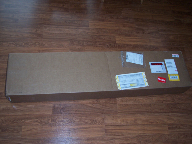Long flat cardboard shipping box with shipping labels on a wood laminate floor