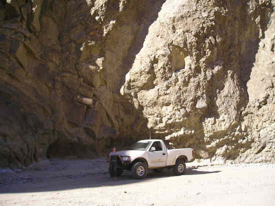 White single-cab pickup parked against a towering rock canyon wall in the desert