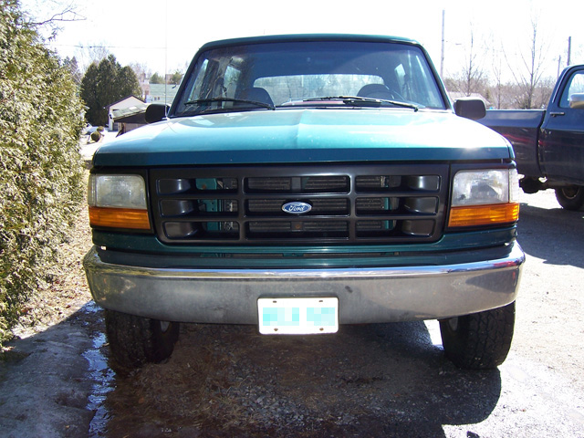 Front view of a teal-green 1990s Ford F-series pickup with FORD grille parked on a snowy lot