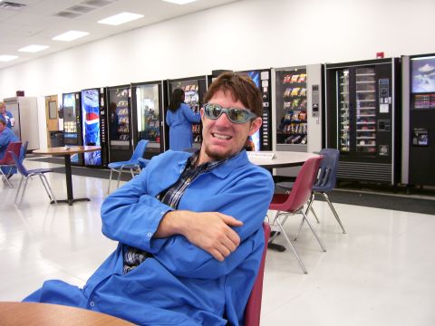 1994 Ford Probe - A man wearing a blue coat and sunglasses smiles while sitting in a break room with vending machines in the background.