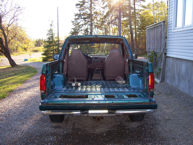 Rear tailgate-down view into the bed and cab of a teal Ford pickup