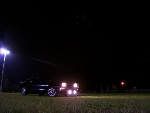 1994 Ford Probe - A black coupe with pop-up headlights is parked on a grassy field under bright lights at night.