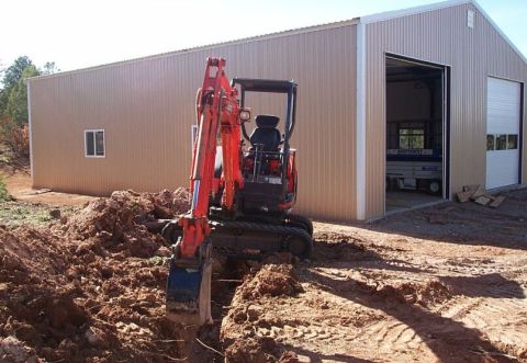 1986 Ford Ranger - An excavator is actively digging a trench in front of a large metal building.