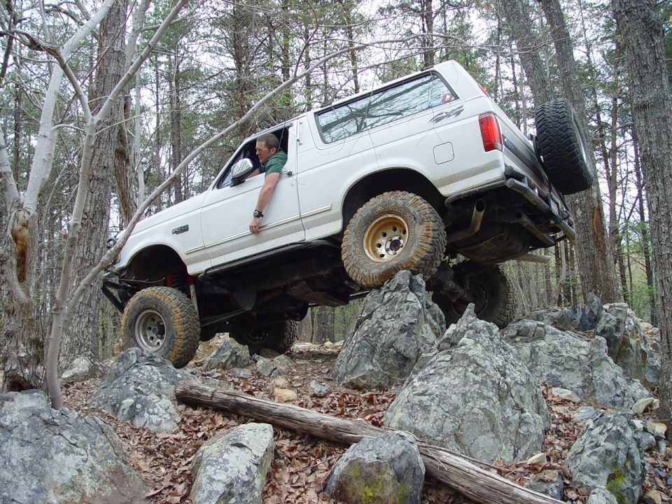White 1996 Ford Bronco climbing over large rocks on a wooded trail