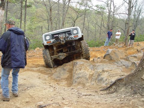 1996 Ford Bronco - A modified white off-road vehicle navigates a rocky trail with spectators watching.