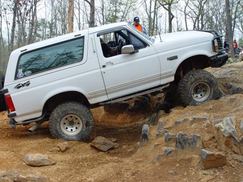 1996 Ford Bronco - White 1996 Ford Bronco navigating a rocky obstacle on an off-road trail.