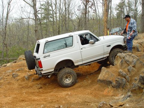 1996 Ford Bronco - A white Ford Bronco navigates a rocky off-road course with a man watching.