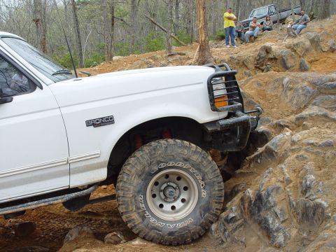 1996 Ford Bronco - A white 1996 Ford Bronco navigates a rocky trail, with another truck and spectators in the background.