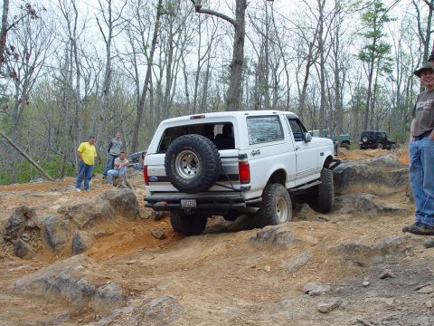 1996 Ford Bronco - A white 1996 Ford Bronco tackles a challenging off-road course with spectators watching.