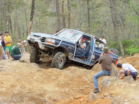 1996 Ford Bronco - A modified blue SUV navigates a challenging off-road course with spectators watching.
