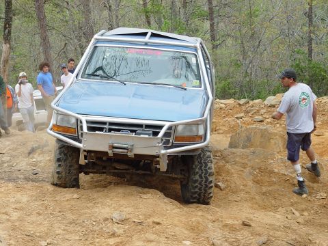 1996 Ford Bronco - A blue 1996 Ford Bronco navigates a challenging off-road course with spectators nearby.
