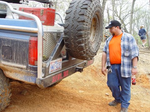 1996 Ford Bronco - A man stands next to the rear of a blue Ford Bronco with a large spare tire mounted on the back.