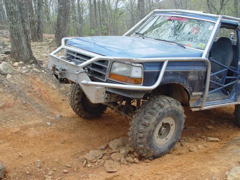 1996 Ford Bronco - This modified SUV is navigating a rocky, off-road trail in a wooded area.