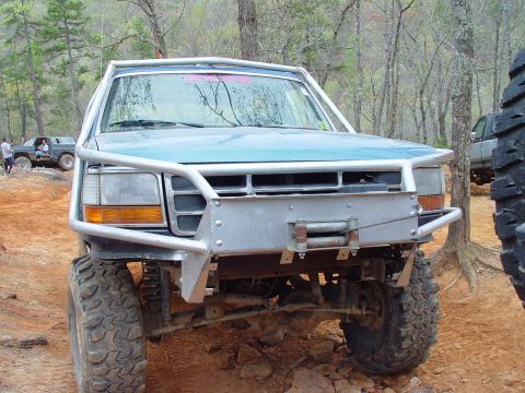 1996 Ford Bronco - A modified blue Ford Bronco is shown off-road with a custom bumper and winch.